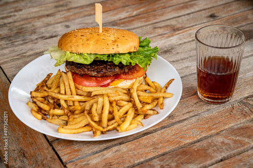 Hamburger and fries. Tasty burger with cheese, lettuce, beef and tomatoes served outdoor on a wooden table with a glass of coca.