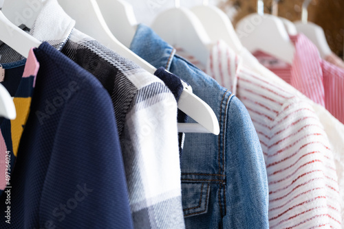 Wooden white hangers with clothes on the rail in the store with women's clothing for sale. Shirt, dress, jacket, vest, jeans. Flea market, second hand, discount, exchange, donation photo