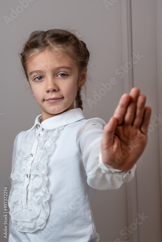 Little strict serious confident kid girl in white blouse showing stop gesture with palm refusing say no