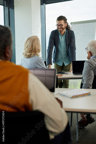 Young hipster educator teaching a multicultural group of senior students how to use the internet in the classroom.
