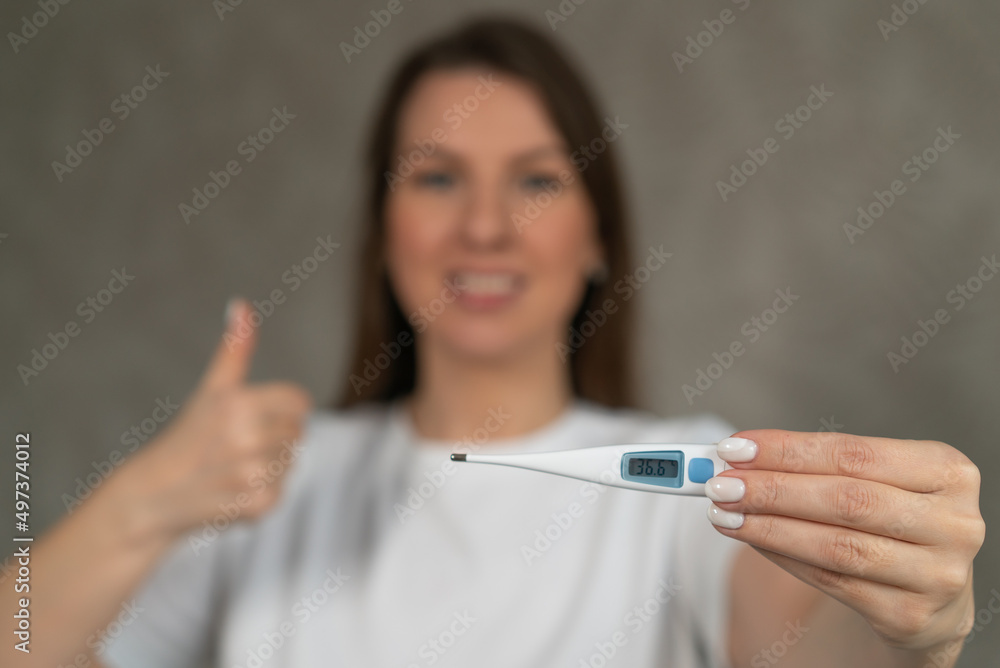 Woman holds an electronic thermometer in her hands, showing 36.6 degrees Celsius Woman holds an electronic thermometer in her hands, showing 36.6 degrees Celsius