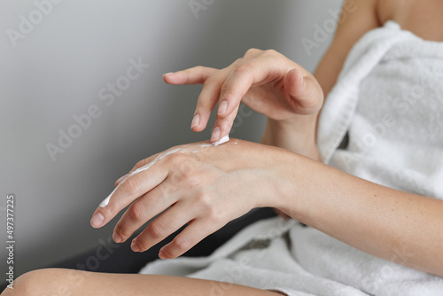 Hands of a young girl with cream. A young girl in towels smears her hands with close-up cream. A girl after a shower in a white towel. Applying the cream to the hands close-up.