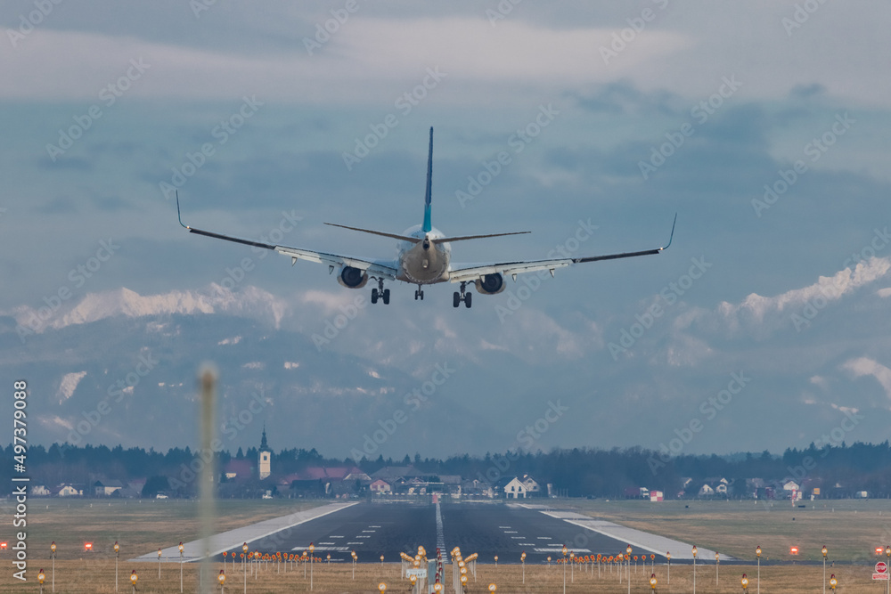 Rear view of modern twin jet engine descending from the clouds. Low flying passenger jet liner ready to land on an airport of Ljubljana, Slovenia. Rear view of modern twin jet engine descending from the clouds. Low flying passenger jet liner ready to land on an airport of Ljubljana, Slovenia.