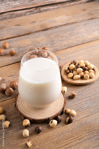 Vegan non diary hazelnut milk in glass with whole hazelnuts on a linen napkin on a rustic wooden background. Lactose free hazelnut drink is plant based alternative milk. Healthy milk product, close up