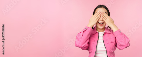 Surprise and celebration. Portrait of asian happy girl close eyes, waiting for gift, anticipating something, standing blindsided against studio background photo