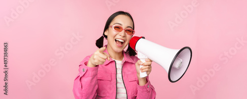 Attention, announcement concept. Enthusiastic asian girl shouting in megaphone, advertising with speaker, recruiting, standing over pink background