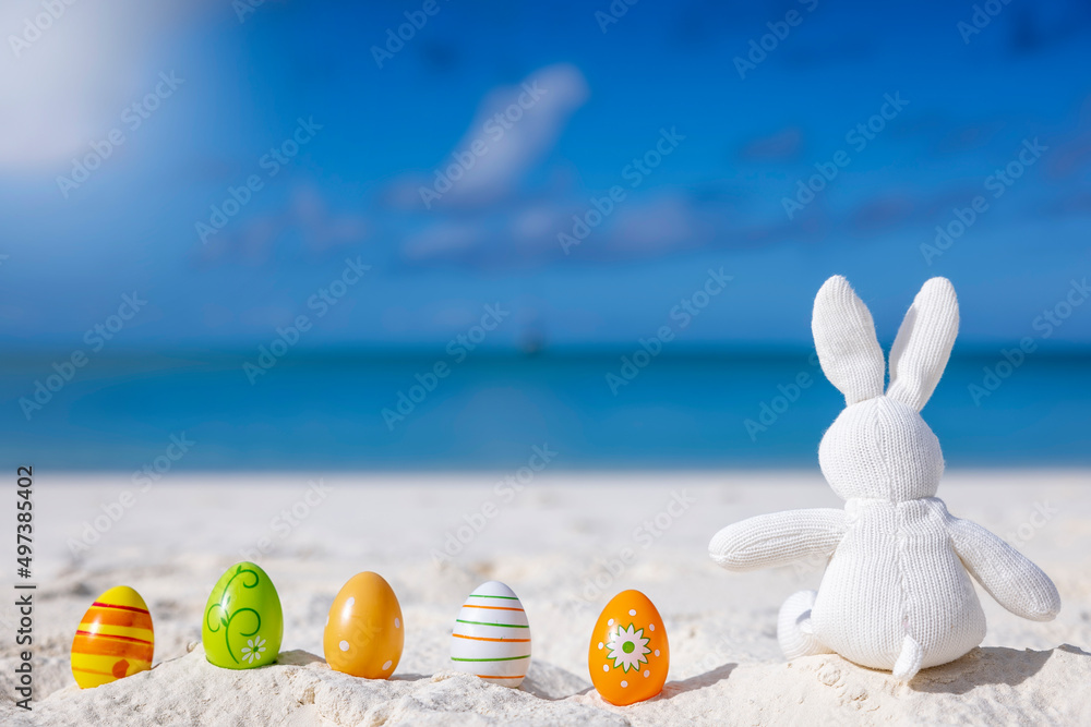 Easter travel concept with a bunny and colorful eggs sitting in the sand on a tropical paradise beach