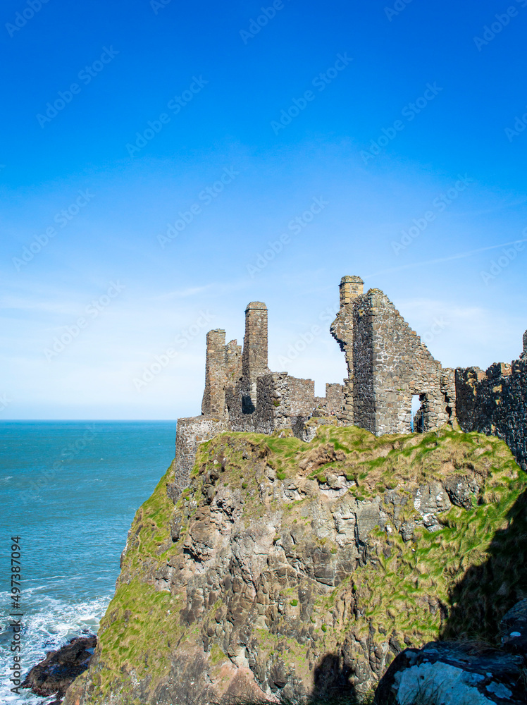 Famous Dunluce Castle on the cliff with blue sea background in a sunny day. Famous Dunluce Castle on the cliff with blue sea background in a sunny day.
