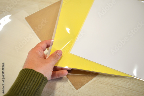 Worker grabbing some laminating pouches with yellow, craft and white sheets inside the plastic. photo