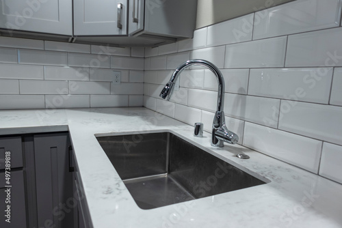 Angled view of a white  empty kitchen with marble countertops and a gas stove  the faucet in view in the background