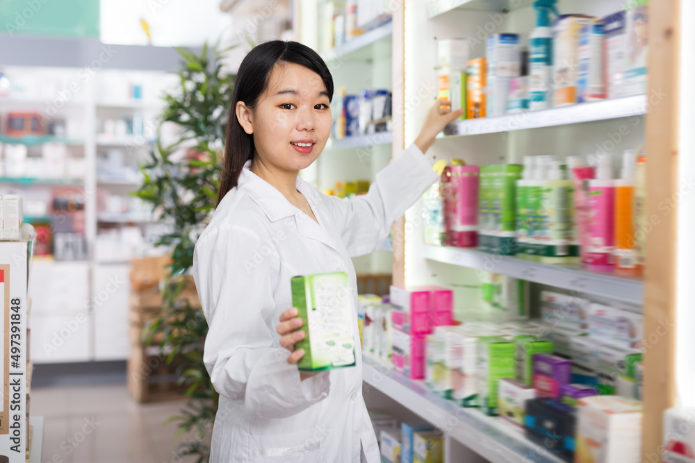 Focused Chinese pharmacist is searching medicines on shelves in drugstore