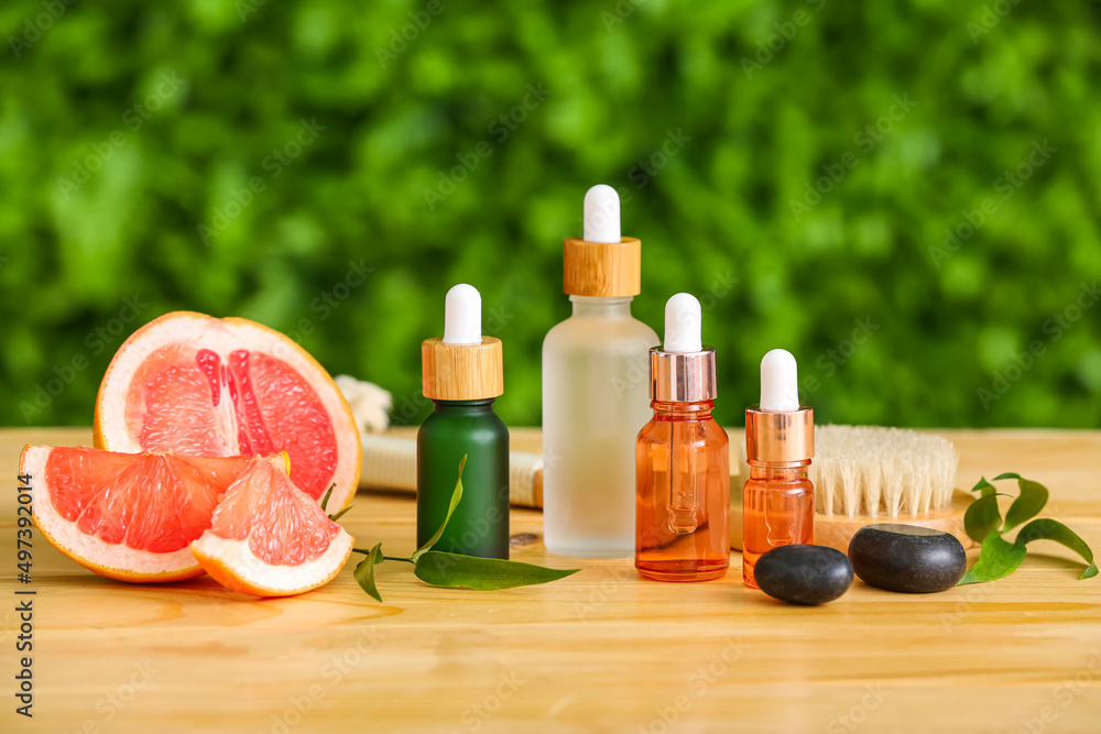 Composition with bottles of essential oil, grapefruit and massage brush on table outdoors Composition with bottles of essential oil, grapefruit and massage brush on table outdoors