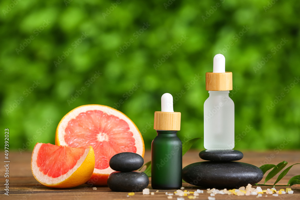 Composition with bottles of grapefruit essential oil and spa stones on wooden table outdoors Composition with bottles of grapefruit essential oil and spa stones on wooden table outdoors