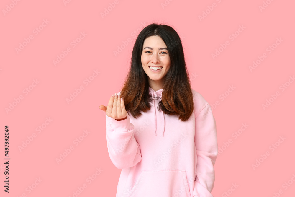 Young Asian woman in hoodie on pink background