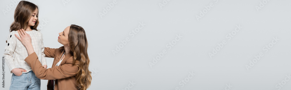 woman with long hair looking at child holding hand in pocket isolated on grey, banner. woman with long hair looking at child holding hand in pocket isolated on grey, banner.