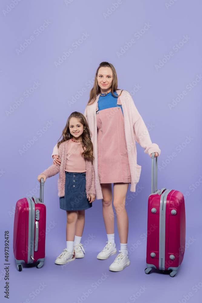 full length of happy mother and child standing near baggage on purple. full length of happy mother and child standing near baggage on purple.