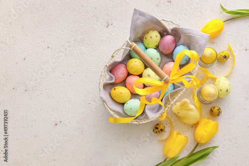 Basket with painted Easter eggs, tulip flowers and bunny on light background