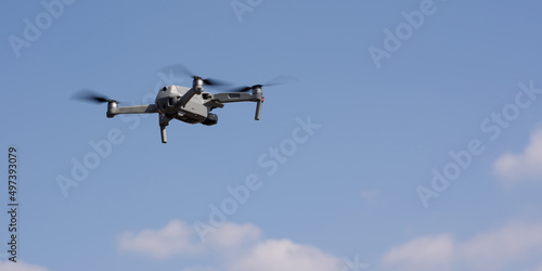 A modern quadcopter with a high resolution camera hovering in the air. A compact gray RC drone takes aerial photo or video footage from the air. Gadget in flight against the blue sky. Drone control.