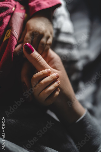 baby hold her mothers hand while sleep close up on hand of small infant baby girl holding thumb of her mother unknown while sleep at night in dark room childhood bonding care and motherhood concept