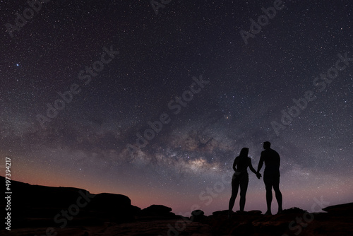 Milky Way with silhouette of people. Landscape with night starry sky. Standing man and woman on the mountain with yellow light. Beautiful galaxy. Universe.