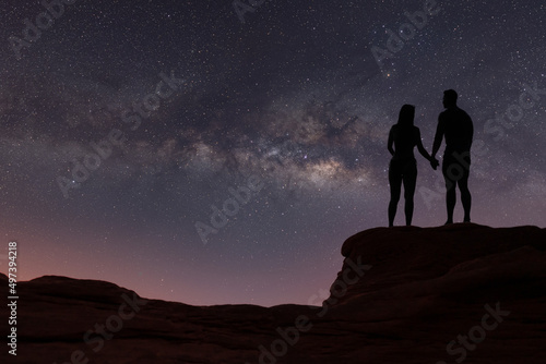 Milky Way with silhouette of people. Landscape with night starry sky. Standing man and woman on the mountain with yellow light. Beautiful galaxy. Universe.