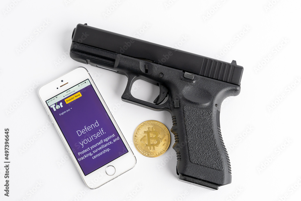 DRESDEN, GERMANY - 19. March 2021: Tor browser on a smartphone, a pistol  and a Bitcoin as