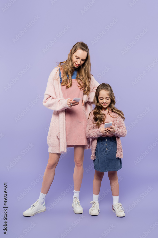 full length of mother and daughter using gadgets on purple. full length of mother and daughter using gadgets on purple.