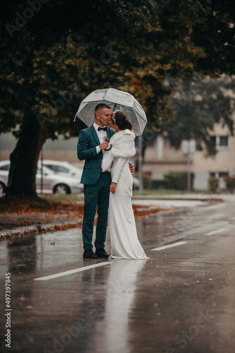Wedding happy moments. Happy young couple, newlyweds walking the streets in rainy weather while carrying an umbrella.