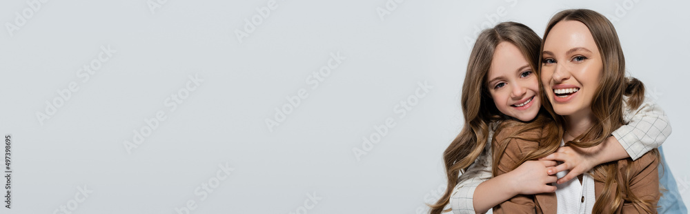 happy girl embracing happy mom while looking at camera isolated on grey, banner. happy girl embracing happy mom while looking at camera isolated on grey, banner.