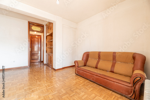 Living room with an old three-seater sofa with oak parquet floors and wooden shelves embedded in the wall