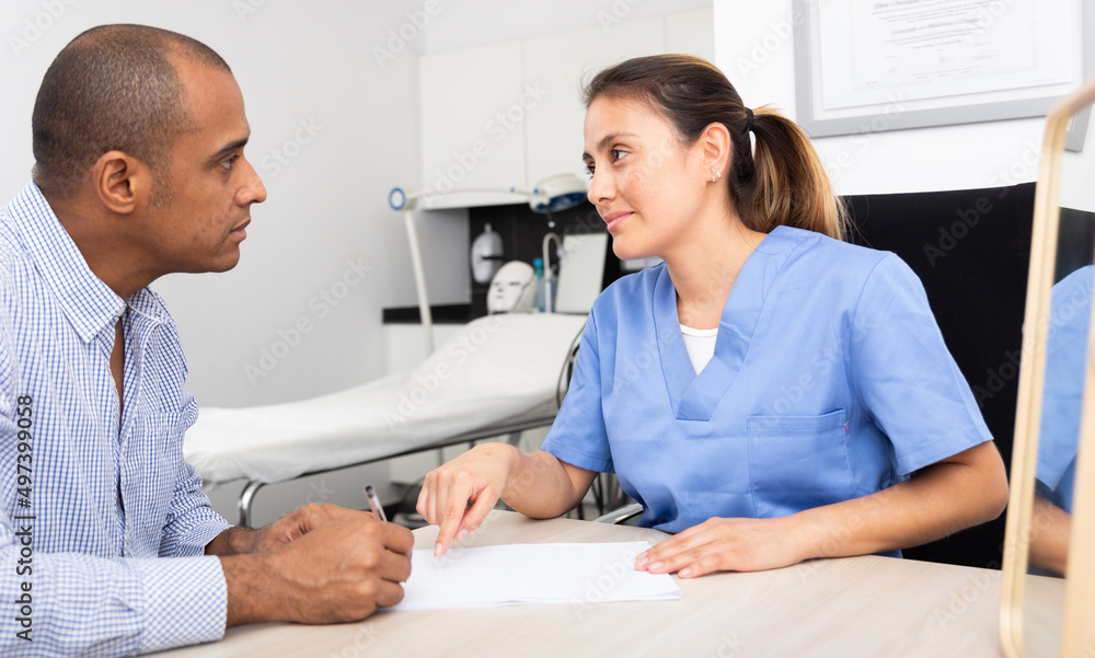 Fototapeta premium Portrait of professional colombian female cosmetologist planning upcoming treatments for male patient in modern aesthetic medicine office