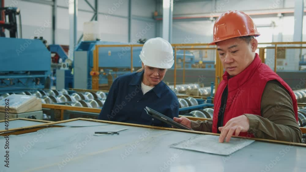 Industry engineers man and woman with helmet checking production process in factory. Hard industries. Manufacturing. Walking in warehouse Industry engineers man and woman with helmet checking production process in factory. Hard industries. Manufacturing. Walking in warehouse
