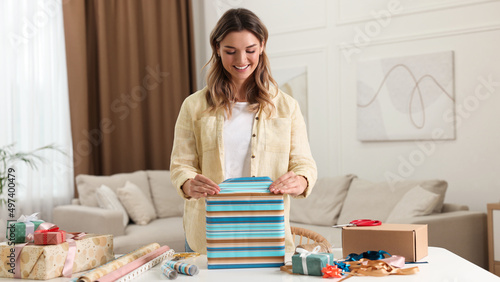 Beautiful young woman wrapping gift at table in living room