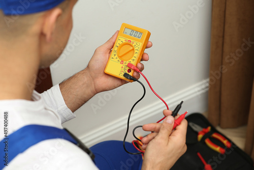 Professional electrician with voltage tester indoors, closeup photo
