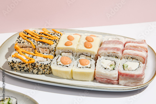 Sushi set on ceramic dishware with coloured chopsticks. Trendy set of maki sushi in minimal style. Modern japanese menu concept. Maki sushi assorted on coloured background.