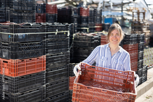 Woman stacking plactic crates in a greenhouse photo