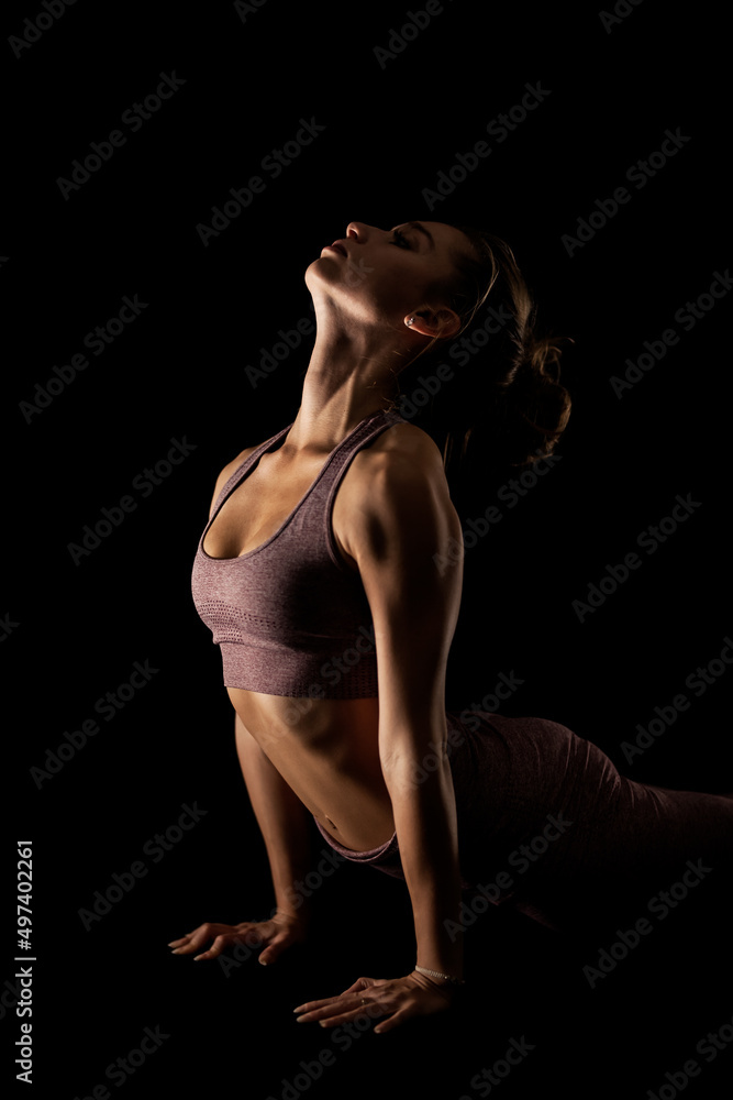 Fit woman practicing yoga poses. Side lit half silhouette girl doing exercise in studio against black background..