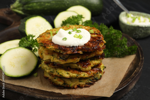 Delicious zucchini fritters with sour cream served on black table, closeup