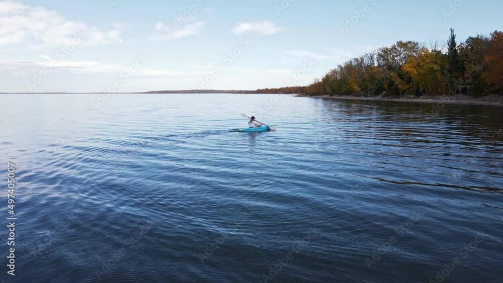 Clear blue buffalo lake in southern Alberta during autumn. Aerial footage of a person in a blue kayak paddling along Clear blue buffalo lake in southern Alberta during autumn. Aerial footage of a person in a blue kayak paddling along