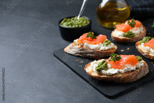 Delicious bruschettas with cream cheese, salmon and pesto sauce on black table, closeup. Space for text