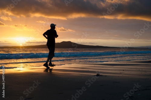 Silhouette man running on Takapuna beach at sunrise, Rangitoto Island in the background, Auckland.