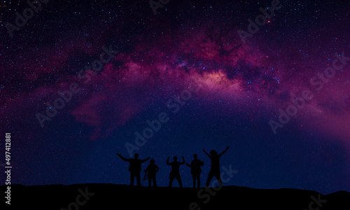 A group of people are happily standing next to the Milky Way galaxy pointing at a bright star.