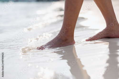 Closeup image of woman with barefoot while walking on the white beach and the sea