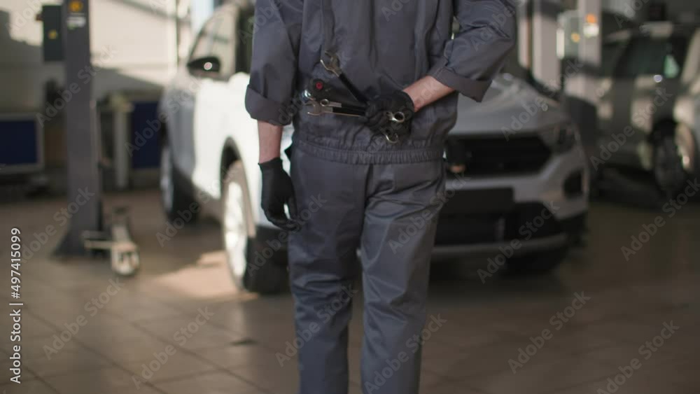 automobile maintenance, a professional male locksmith in uniform stands with tools in his hands to inspect or repair car in service center, rear view automobile maintenance, a professional male locksmith in uniform stands with tools in his hands to inspect or repair car in service center, rear view
