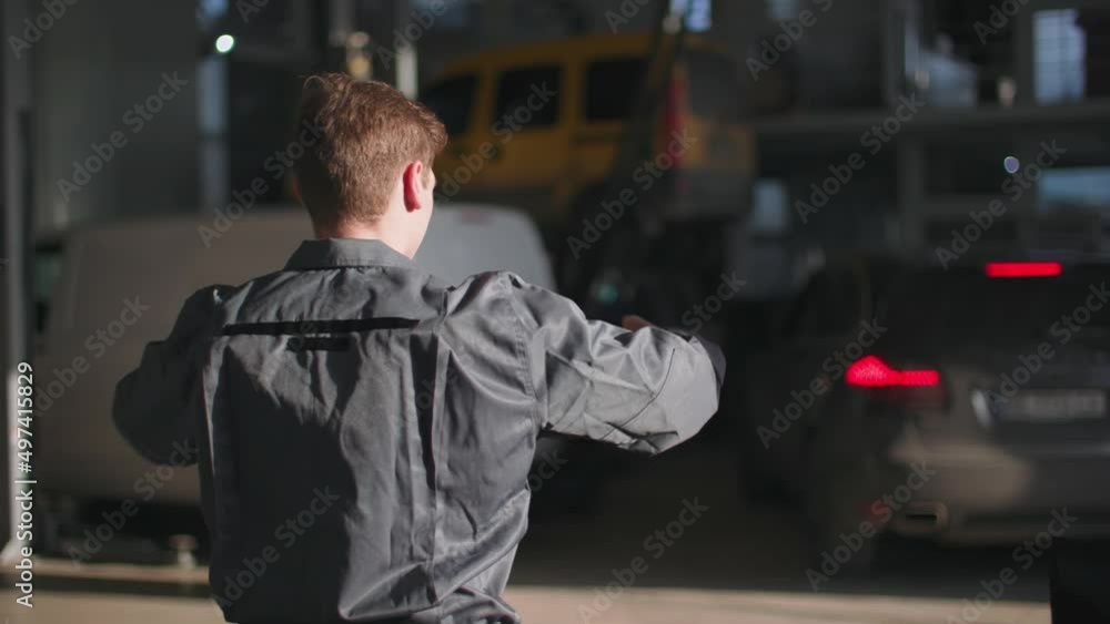 young male mechanic in uniform regulates movement of a car during a check-in at a site for technical inspection in a car service, rear view