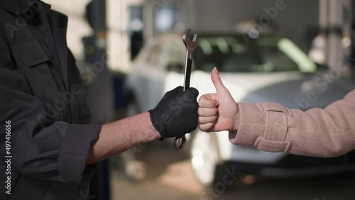 intenance, a car mechanic with a wrench in his hands raises his hand along with a satisfied female colleague shows a thumbs up, good service concept, close-up photo