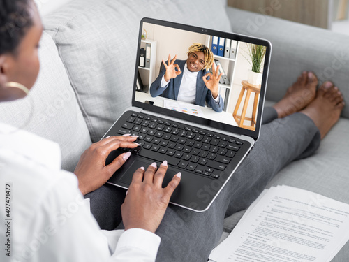 Video call. Remote work. Online negotiation. Relaxed business woman using laptop discussing agreement online with male partner on screen in virtual home office.