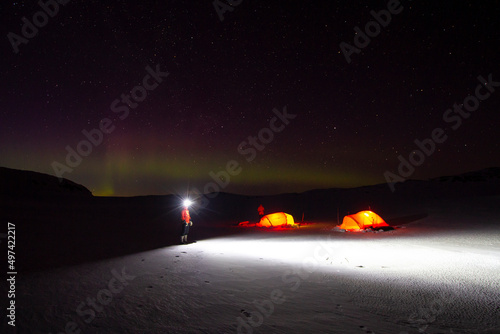 Man standing outside the tent under the Northern lights  in the winter night