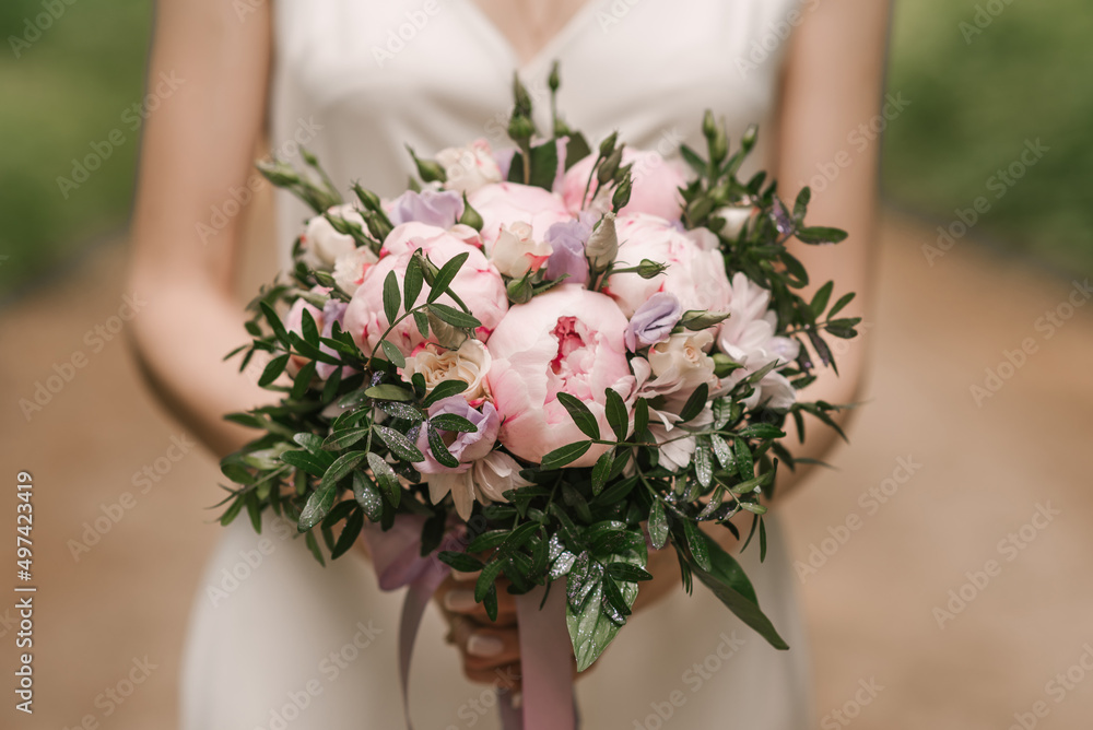A luxurious wedding bouquet with pink peonies in the hands of the bride A luxurious wedding bouquet with pink peonies in the hands of the bride
