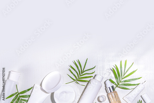 Beauty cosmetic skincare products on white background with tropical palm leaves flatlay copy space. Set of white jars, tubes, droppers and bottles. Summer spa, daily natural skin care routine concept